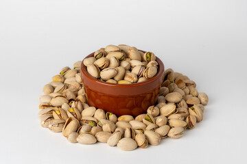 Salted pistachios in a glass bowl and scattered around on a white background, isolated, side view, crunchy roasted nuts,tasty,nutritious snack, healthy organic food, high-protein vegetarian ingredient