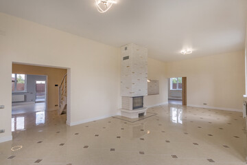 Large empty living room with final finishing in a private house. Light floor tiles, fireplace .Unfurnished.