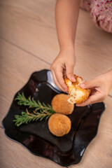 Aperitivo gourmet: bolas de queso crujientes sobre mesa rústica, Manos comiendo.