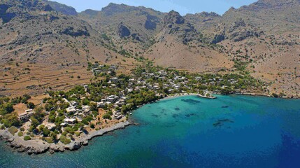 Fototapeta premium Aerial view of Greek village nestled on coastline with turquoise water and mountains