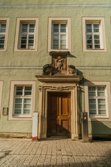 Building facade with a wooden door and decorative stone elements. Architectural detail, European architecture. "Das Diak." signage, educational center, sunlight and shadow.
