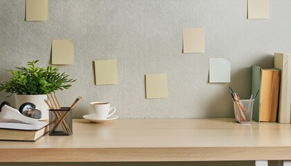 wooden desk with stationery, books, mug, a plant and post-its on the wall, copy space