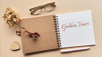 Open scrapbook with text Golden Years on a white page, surrounded by dried flowers, wooden heart,...
