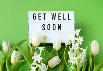 Lightbox with text Get Well Soon surrounded by white tulips and hyacinths on a green background,...