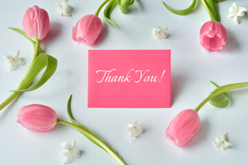 Pink tulips and white flowers arranged around a red card with the text Thank You on a white...