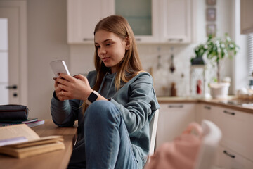 Smiling female student using cell phone while learning at home.