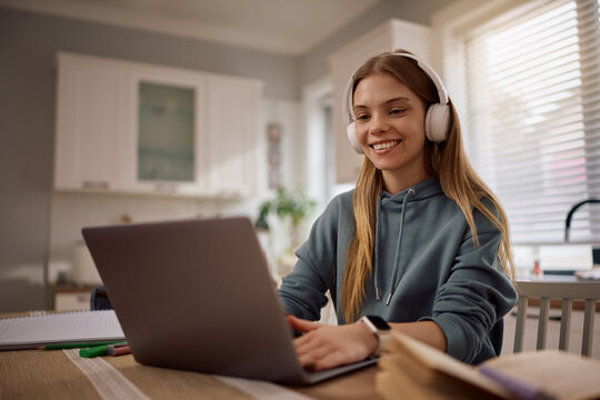 Happy female student making video call over laptop while e-learning at home.