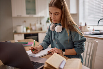 Female student taking notes while e-learning at home.