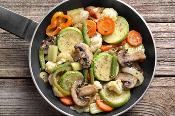 Different vegetables and mushrooms in frying pan on wooden table, top view