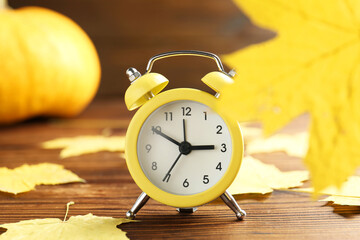 Autumn time. Alarm clock and golden leaves on wooden table