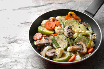Different vegetables and mushrooms in frying pan on grey textured table, closeup