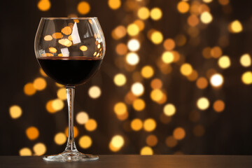 Tasty red wine in glass on table against dark background with blurred lights, bokeh effect. Space for text