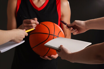 Sportsman signing autograph on basketball ball against black background, closeup