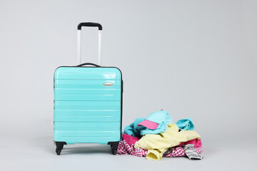 Suitcase and messy pile of clothes on light grey background. Space for text