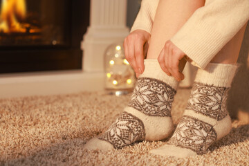 Woman in warm socks resting near fireplace at home, closeup. Space for text