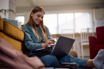Happy female student using laptop while learning at home.