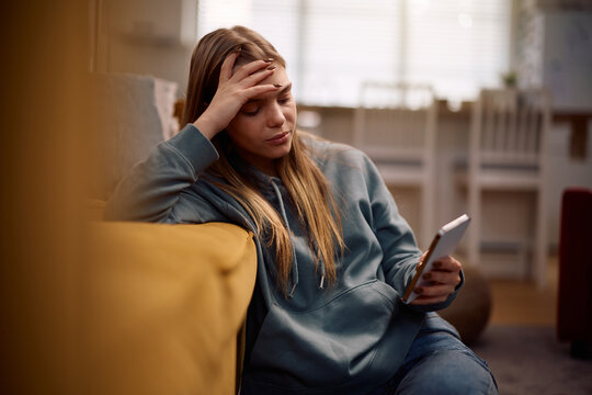 Sad teenage girl reading text message on mobile phone at home.
