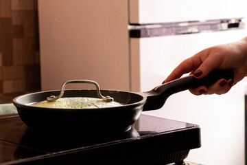 Girl holding frying pan in kitchen on induction hob and cooking