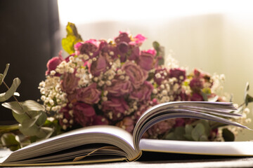 Open book on wooden table at home with dry roses bouquet