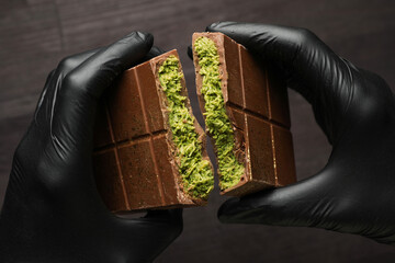 Woman breaking Dubai chocolate bar with pistachio and knafeh at dark table, closeup