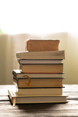 A stack of books lies on a wooden table at home