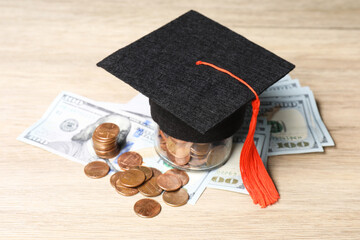 Graduate hat, dollar banknotes and coins on wooden table, closeup. Tuition payment