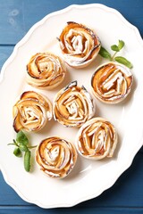 Tasty apple roses with powdered sugar served on blue wooden table, top view
