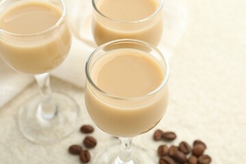 Coffee cream liqueur in glasses and beans on white table, closeup