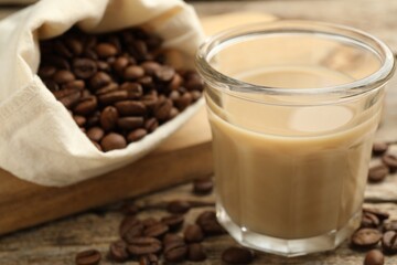 Coffee cream liqueur in glass and beans on wooden table, closeup