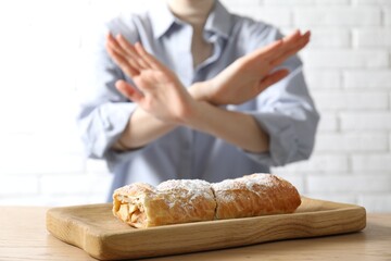 Woman refusing to eat apple strudel at wooden table near white brick wall, selective focus. Food...