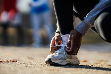 Close up of black sportswoman tying shoelace on sneaker and preparing for sport in nature.