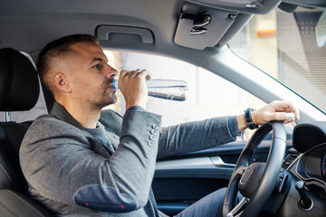 Thirsty smart casual businessman driving a car and drinking bottle of water in a car.