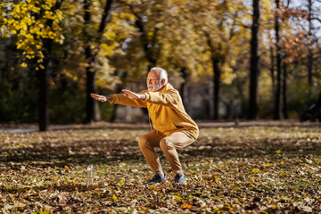 An old active sportsman doing squats in nature.