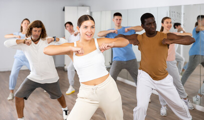 Big group of young adult fit people in activewear exercising together during training in dance...