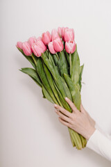 A woman’s hand holds a fresh bouquet of pink tulips against a plain white background. A simple yet elegant symbol of love appreciation and celebration for International Women's Day and Mother's Day.