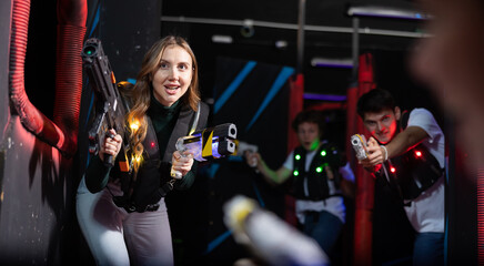 Positive girl holding laser pistol playing laser tag game with his friends