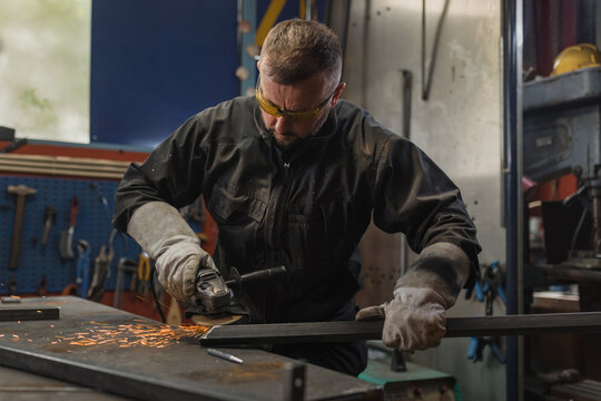 Skilled manual worker wearing protective equipment grinding steel in a welding workshop. Metalwork industry career concept.