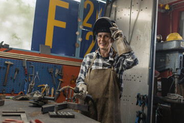 Portrait of woman welder in protective gear working in metal workshop.