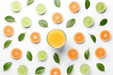Glass of orange juice surrounded by lime and orange slices and leaves on white background.