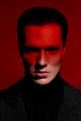 Close Up portrait of a handsome serious young man in black suit over red dark background. Horizontal view. Space for text.