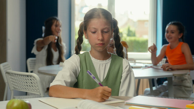 Caucasian teen schoolgirl sad upset kid student pupil studying at desk class school education stress problem cruel laugh children classmates bullying mock girl child abuse bully psychological trauma
