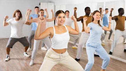 Obraz premium Cheerful energetic multiracial dancers of different ages dancing aerobics at lesson in modern class of gym