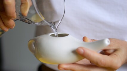 Healthcare professional pouring sterile water into ceramic neti pot, performing nasal irrigation...