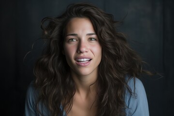Fototapeta premium A woman with long, wavy hair gazes warmly at the viewer, her eyes sparkling with joy. The soft lighting enhances the warmth of her smile in a cozy, dark room