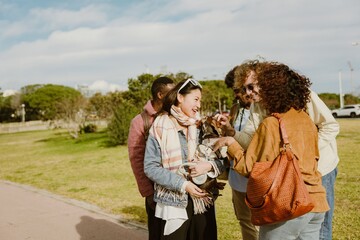 A group of multiracial people is standing outdoors, in the daytime, and several of them are petting...