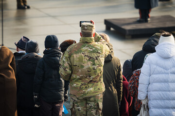 An American soldier in uniform takes a picture on his phone in the crowd at a military parade in...