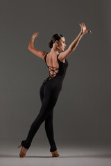 Obraz premium Female dancer in black bodysuit performing contemporary Latin dance pose on gray studio