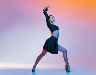 Stylish female dancer in black outfit posing in Latin dance move on vibrant gradient studio background.