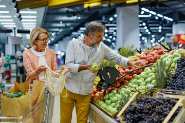 Senior couple choosing apples in supermarket, shopping for groceries together