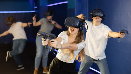 Cheerful emotional young woman in VR headset fully immersed in game, actively engaged in virtual...